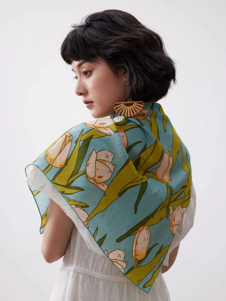 A green tulip floral printed silk square scarf made of 100% mulberry silk, shown draped at the side as a shawl.