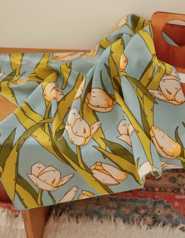 A green tulip floral printed silk square scarf made from 100% mulberry silk, laid flat on a tabletop for display.