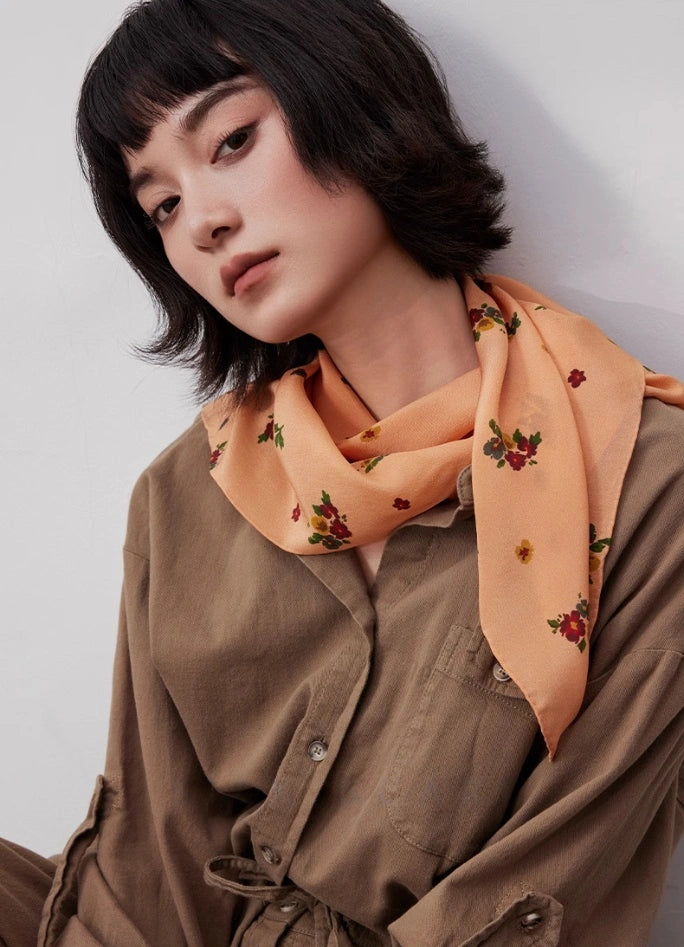 Light orange floral silk square scarf styled as a neck accessory, demonstrating its elegance and versatility.