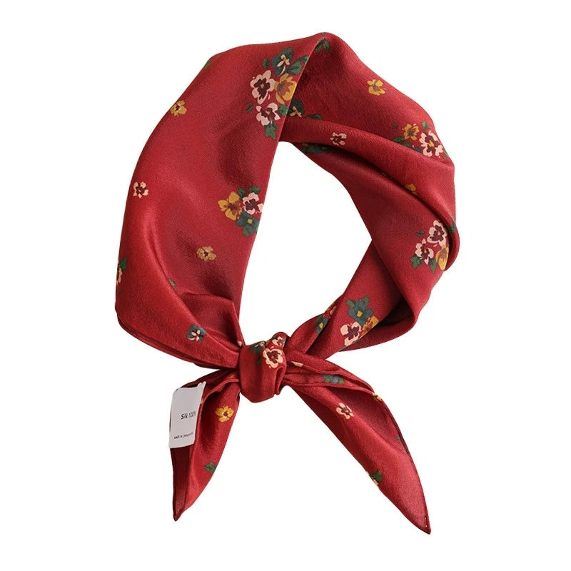 A close-up of a red silk square scarf with a floral print highlights the delicate floral pattern and luxurious silk material.